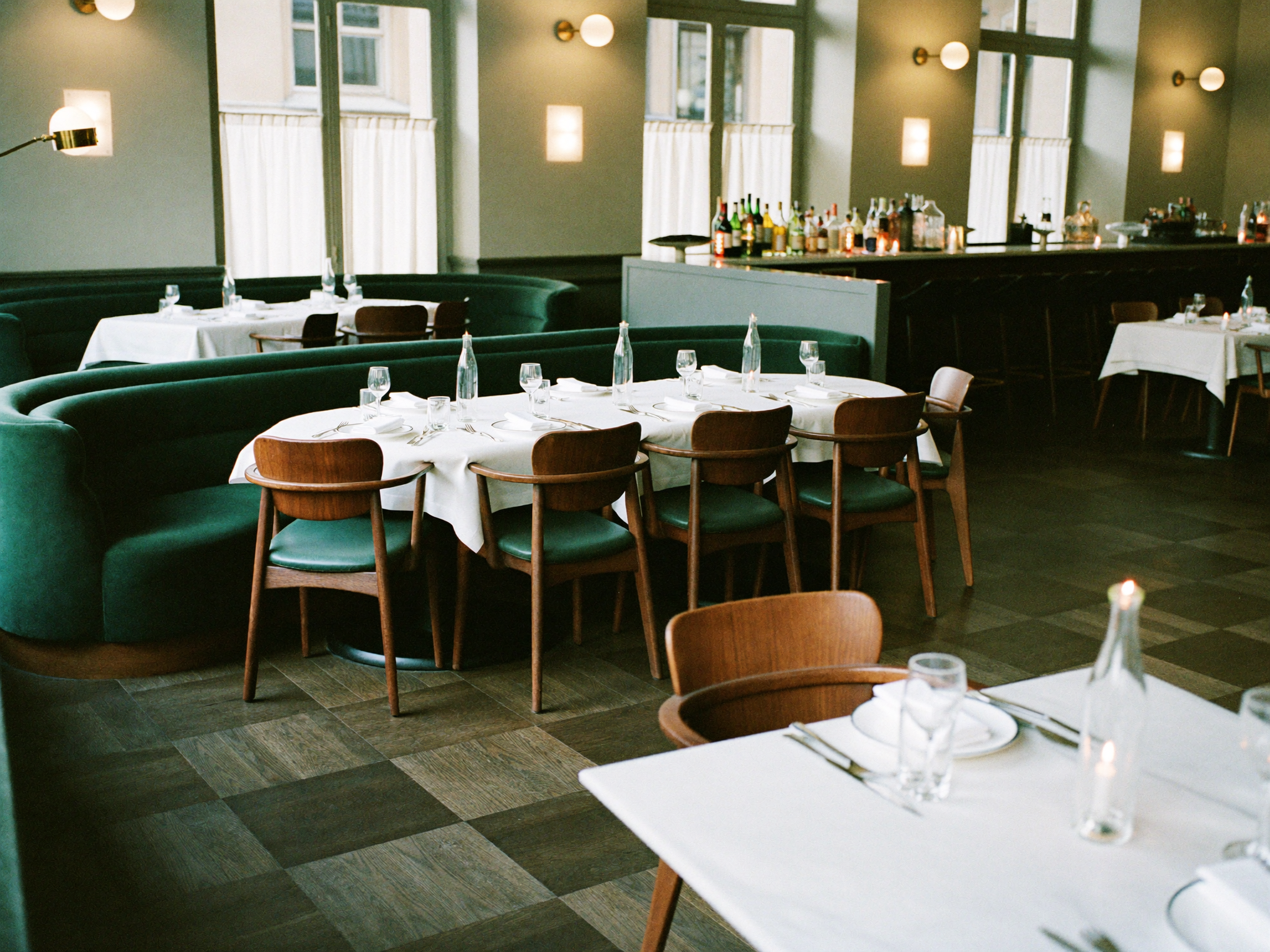 Elegant restaurant med grønne fløyelssofaer og hvite duker