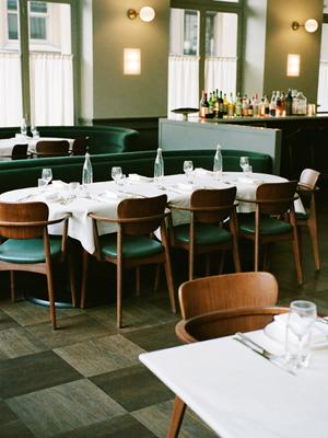 Elegant restaurant med grønne fløyelssofaer og hvite duker