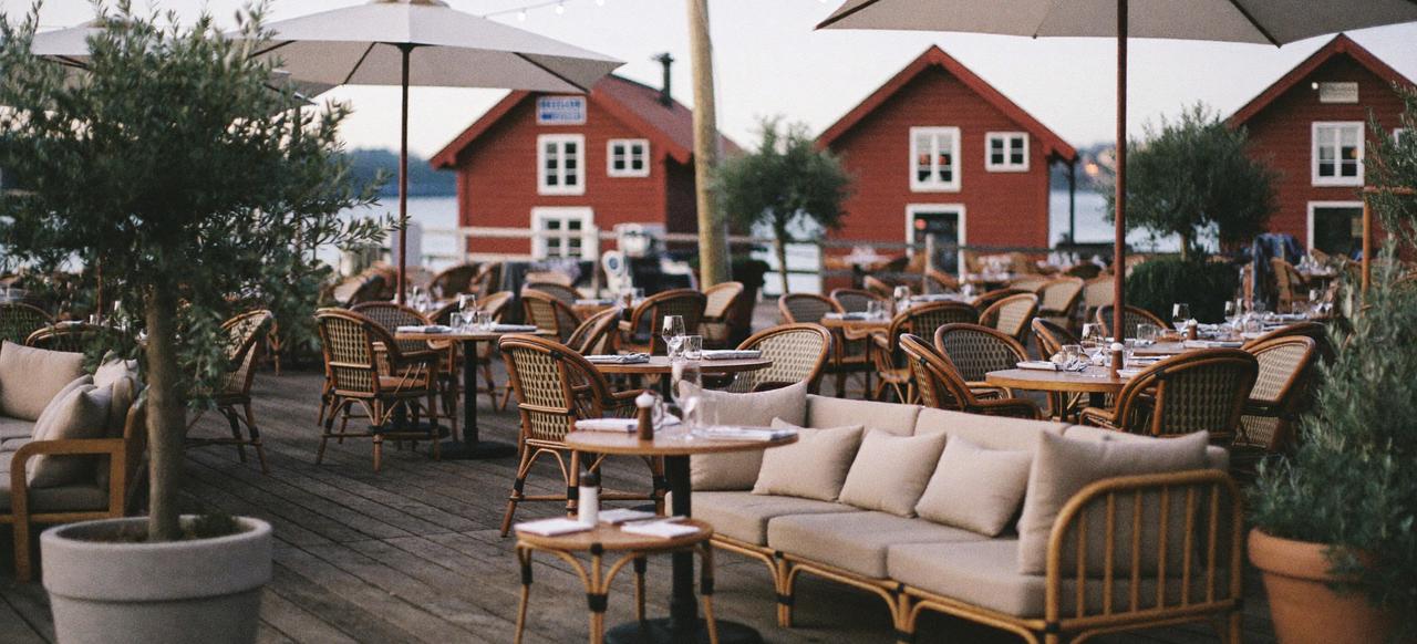 Uteservering på en brygge, møblert med rottingstoler og loungesofaer