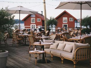 Uteservering på en brygge, møblert med rottingstoler og loungesofaer